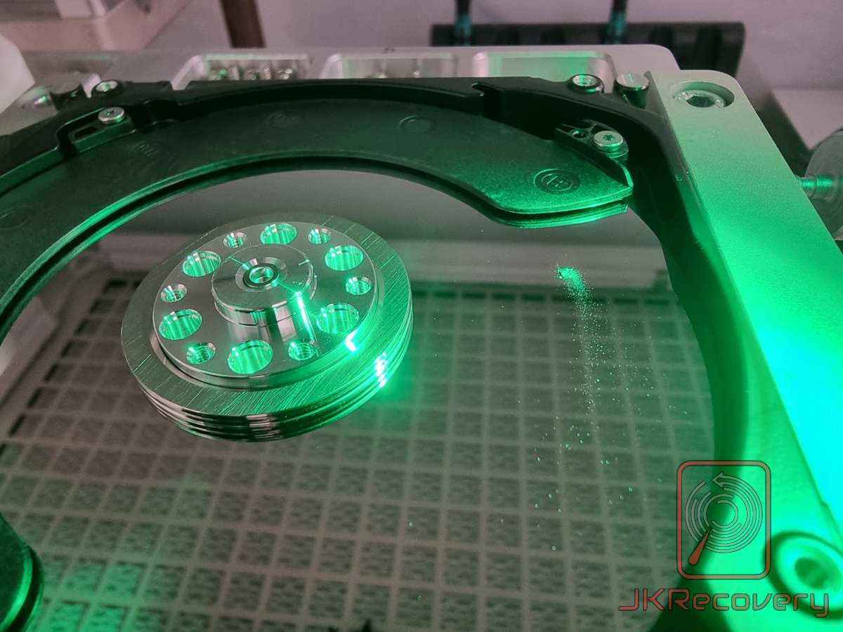 Wnętrze otwartego dysku twardego HDD oświetlone zielonym światłem UV, widoczny talerz magnetyczny bez głowicy odczytu/zapisu oraz mechanizm ramienia aktuatora